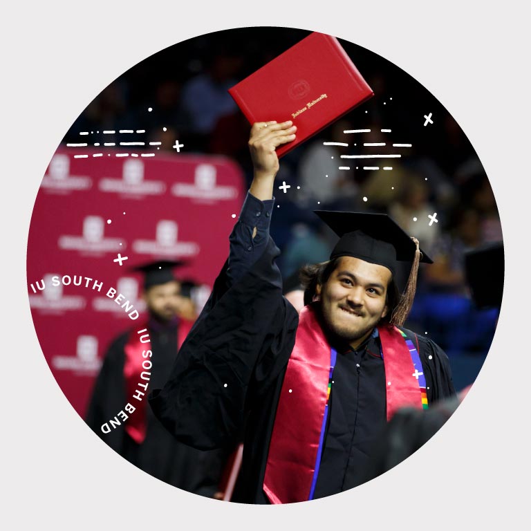 an IU South Bend graduate holds his IU degree high in the air.